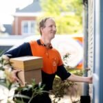Een PostNL-pakketbezorger bij een woning; illustratieve bedrijfsfoto